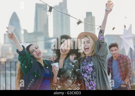 Portrait exuberant young women cheering and drinking at rooftop party Stock Photo