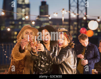 Portrait enthusiastic young adult friends toasting champagne flutes at nighttime rooftop party Stock Photo