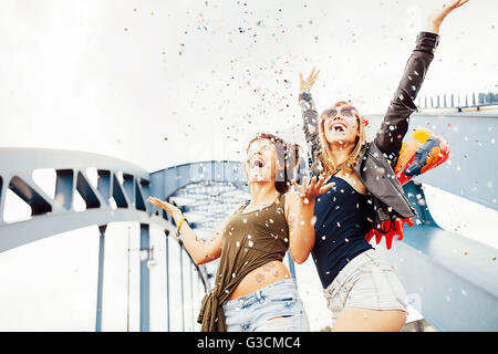 Two young women throwing confetti into the air and looking up, Stock Photo