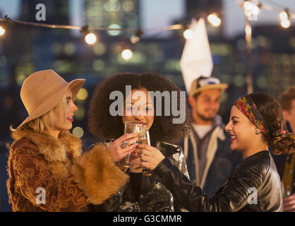 Young women toasting champagne glasses at nighttime rooftop party Stock Photo