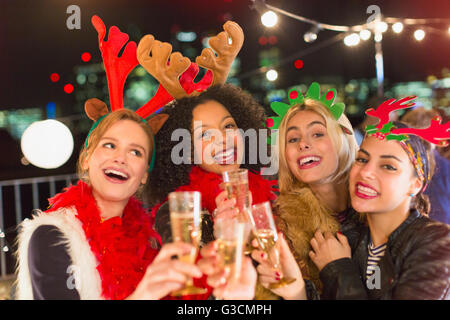 Portrait enthusiastic young women wearing Christmas reindeer antlers and drinking champagne at party Stock Photo