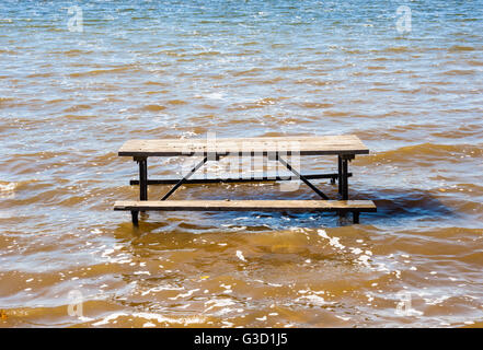 Empty picnic table sinking in wavy muddy brown water. Stock Photo