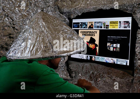 male conspiracy theory believer wearing tin foil hat looking at web sites on a computer screen Stock Photo