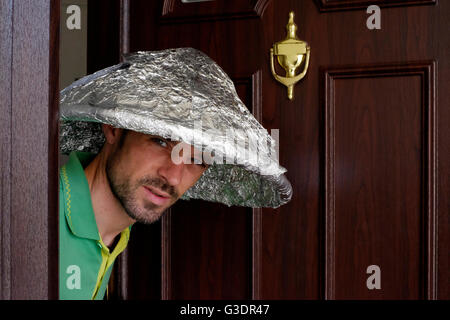 male conspiracy theory believer wearing tin foil hat peering out of doorway Stock Photo