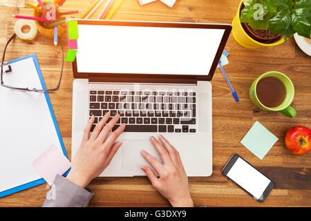 Young woman working with laptop placed on wooden desk with blank screen for text. Shot from aerial view Stock Photo