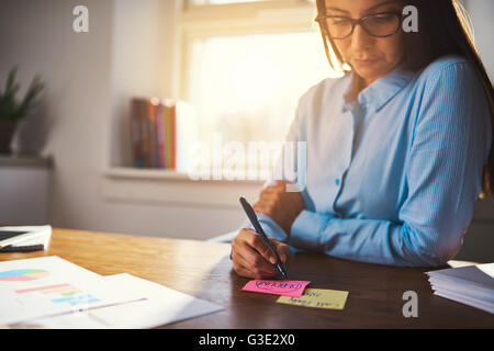 Business woman writing notes on sticky note in pink and yellow colours Stock Photo