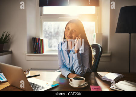 Female entrepreneur talking on the phone sitting at desk like small shop owner Stock Photo