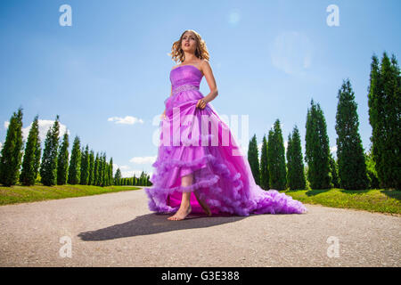 Blonde woman in beautiful pink dress on alley Stock Photo