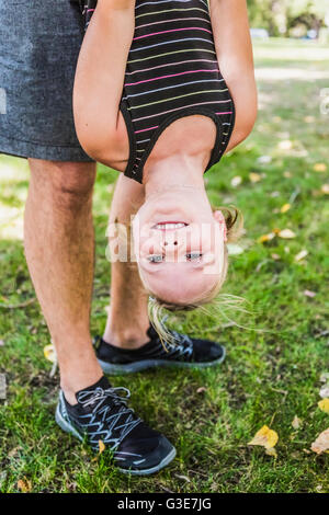 A father hanging his daughter upside down and playing around in a park during a family outing; Edmonton, Alberta, Canada Stock Photo