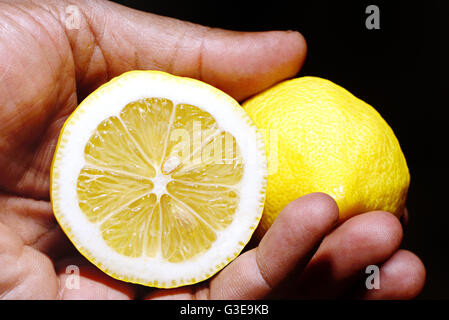 Hand holding two halves of a leamon against a black background Stock Photo