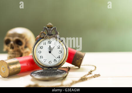 Still life antique clock placed on a wooden floor and a red shotgun shell with human skull on the back. Stock Photo