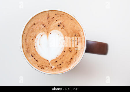 Cup of cappuccino coffee with the milky foam on top in a heart shape viewed from above in a brown cup on white table Stock Photo