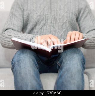 Blind man reading braille book on the couch. Stock Photo
