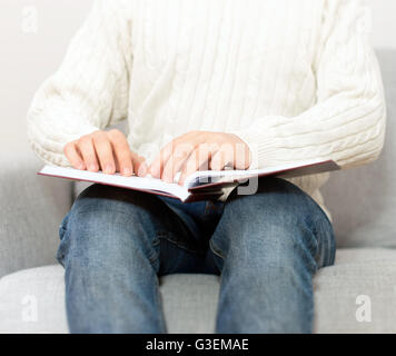 Blind man reading braille book on the couch. Stock Photo