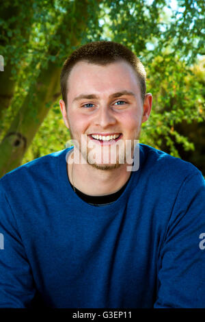 Outdoor portrait of a young man in a long sleeve, blue shirt.  He has blue eyes, short hair and a slight beard. Stock Photo