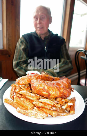 A senior man sitting behind a dinner plate of fish and chips on a table Stock Photo