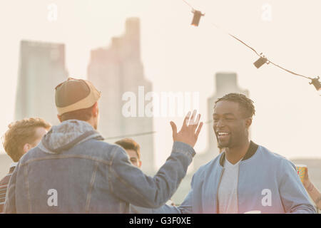 Young men high fiving at rooftop party Stock Photo