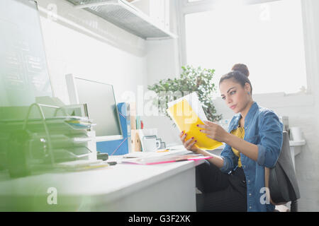 Creative young businesswoman reading paperwork at desk in sunny office Stock Photo
