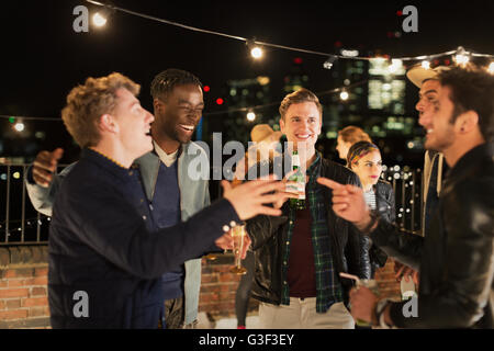 Young men drinking and laughing at rooftop party Stock Photo