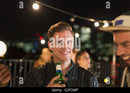 Smiling young man drinking beer at rooftop party Stock Photo