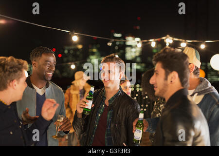 Young men drinking beer and talking at rooftop party Stock Photo