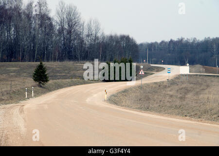 Twisting winding meandering gravel road in meadow with signs near forest Stock Photo