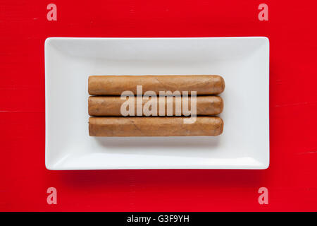 White ceramic dish with luxury Cuban cigars on over red background, rectangle dish Stock Photo