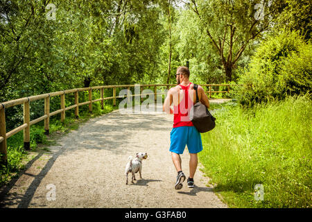 Back portrait of muscular man with bag walking away with pet dog in summer park Stock Photo