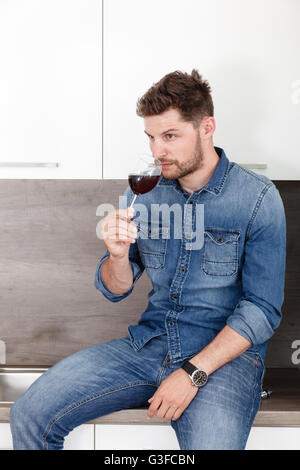 Portrait of a confident man in a denim shirt. A man with a glass of red wine in modern kitchen. Stock Photo