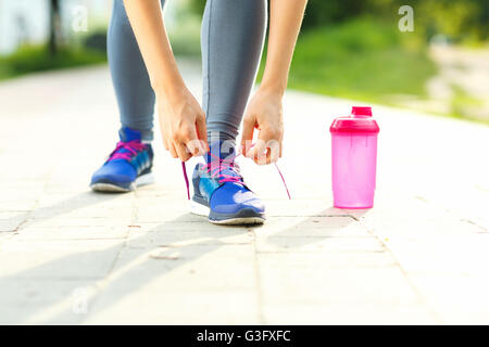 Running shoes - woman tying shoe laces. Closeup of female sport fitness runner getting ready for jogging outdoors in summer Stock Photo