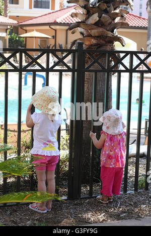 Little girls children standing looking in through a railings wrought iron gate gates Stock Photo