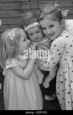 Three blonde kids, children sisters girls cuddled together  in a portrait photo, family fun, togetherness concept, best friends, sibling love joy Stock Photo
