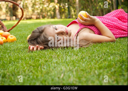 Girl with pink dress lying on back, holding apple Stock Photo