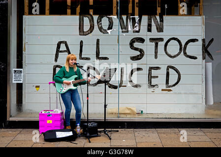 Young woman busking outside an empty store on Princes Street in Edinburgh. Stock Photo