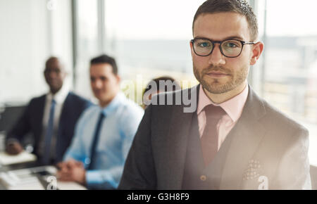 Serious young businessman in a meeting with multiracial colleagues standing looking intently at the camera with sun flare over h Stock Photo