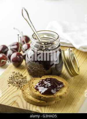 A jar of cherry jam with toast on a wooden board Stock Photo