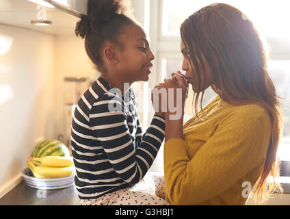 Mother kissing her daughter at home in kitchen, black woman Stock Photo
