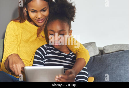 Black mom and daughter learning on tablet sitting at home in sofa Stock Photo