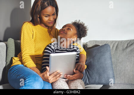 Black mom and daughter with tablet sitting in sofa at home Stock Photo