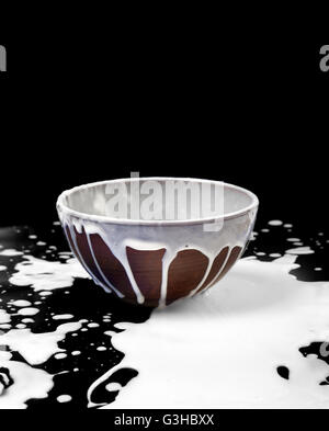 Ceramic bowl and spilled milk in black background with copyspace Stock Photo