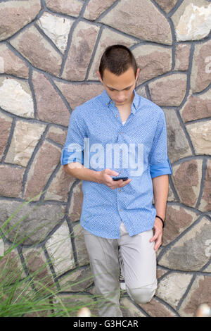 Portrait of cool young man standing against a  wall and reading text message on his cellphone Stock Photo