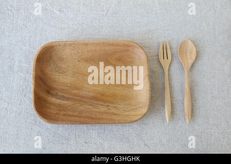 Empty wooden plate with spoon and fork on linen table background Stock Photo