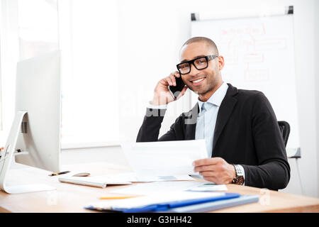 Happy smiling businessman holding documents and talking on mobile phone in the office Stock Photo