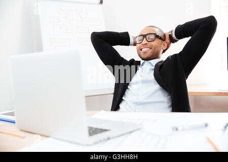 Successful relaxed young businessman sitting back in his chair with hands clasped behind his neck Stock Photo
