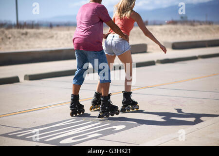 Couple rollerblading outdoors, man holding woman's waist, rear view Stock Photo