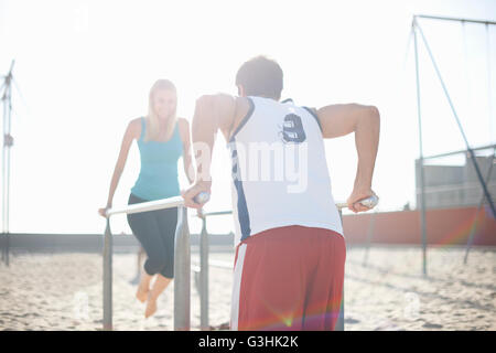 Couple exercising on beach, using gymnastics parallel bars Stock Photo
