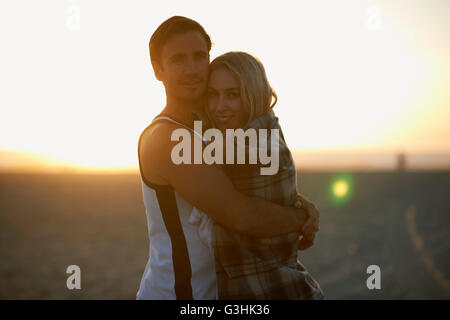 Portrait of couple hugging on beach, at sunset, young woman wrapped in blanket Stock Photo