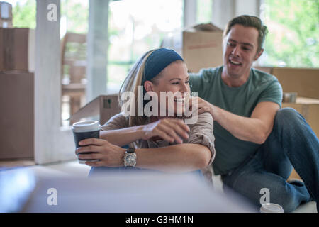 Moving house: Couple taking a break, sitting in room filled with cardboard boxes Stock Photo