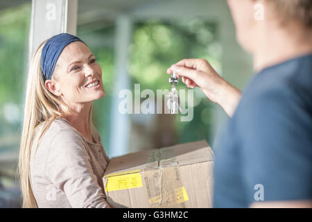 Moving house: woman carrying cardboard box, man holding house keys Stock Photo