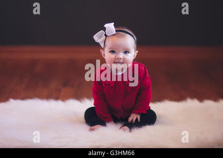 Baby girl sitting on rug wearing bow head band looking at camera mouth open smiling Stock Photo